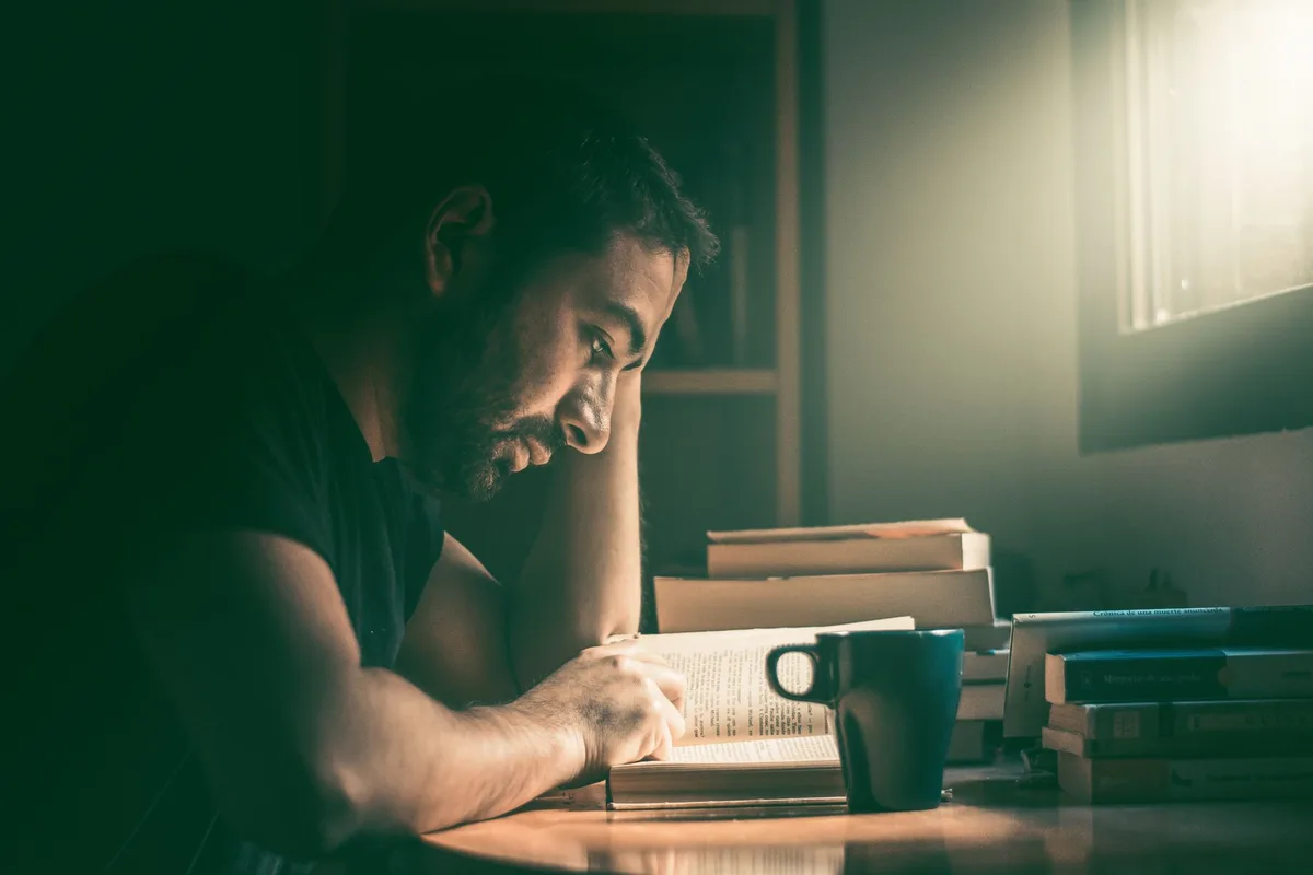 Une personne lisant un livre sur un bureau avec des notes et des ressources pédagogiques.
