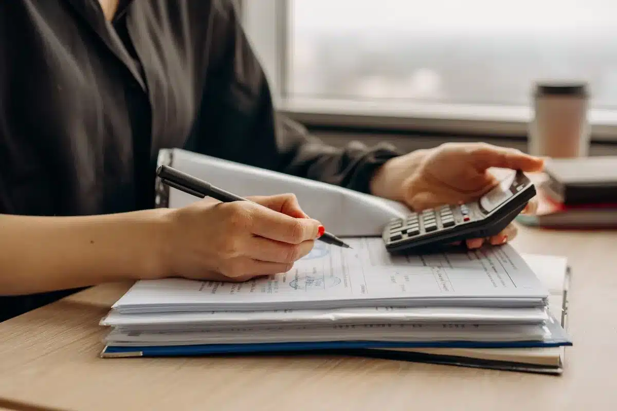 Documents financiers, calculatrice et stylo sur un bureau aux côtés d'un ordinateur affichant un graphique de rendement