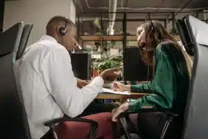 Deux collègues de bureau discutent discrètement à leurs postes de travail dans un environnement professionnel.