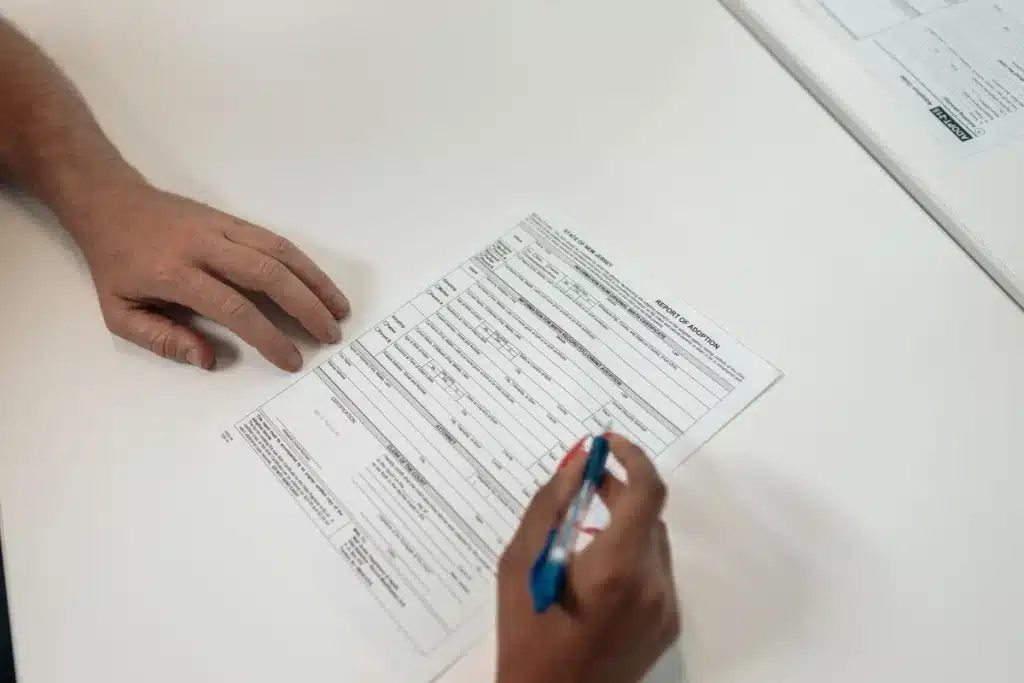 Étudiant complétant un dossier de demande de bourse avec documents fiscaux et ordinateur portable.