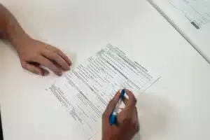 Étudiant complétant un dossier de demande de bourse avec documents fiscaux et ordinateur portable.