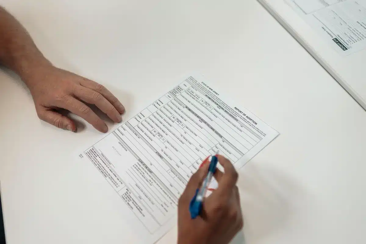 Étudiant complétant un dossier de demande de bourse avec documents fiscaux et ordinateur portable.