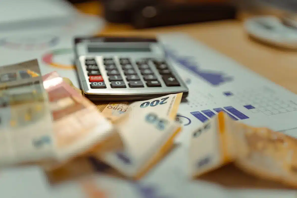 Main de salarié tenant des documents de paie et d'épargne à côté d'un ordinateur affichant des graphiques de croissance