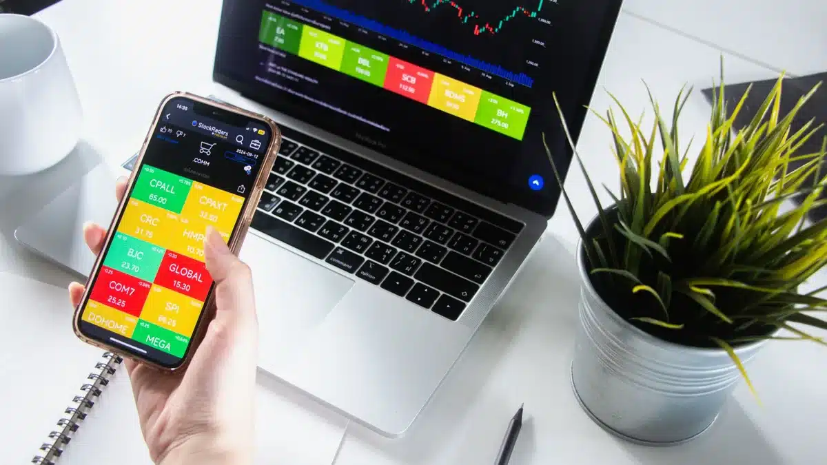 Mains tenant un téléphone affichant une application d'investissement boursier sur un bureau