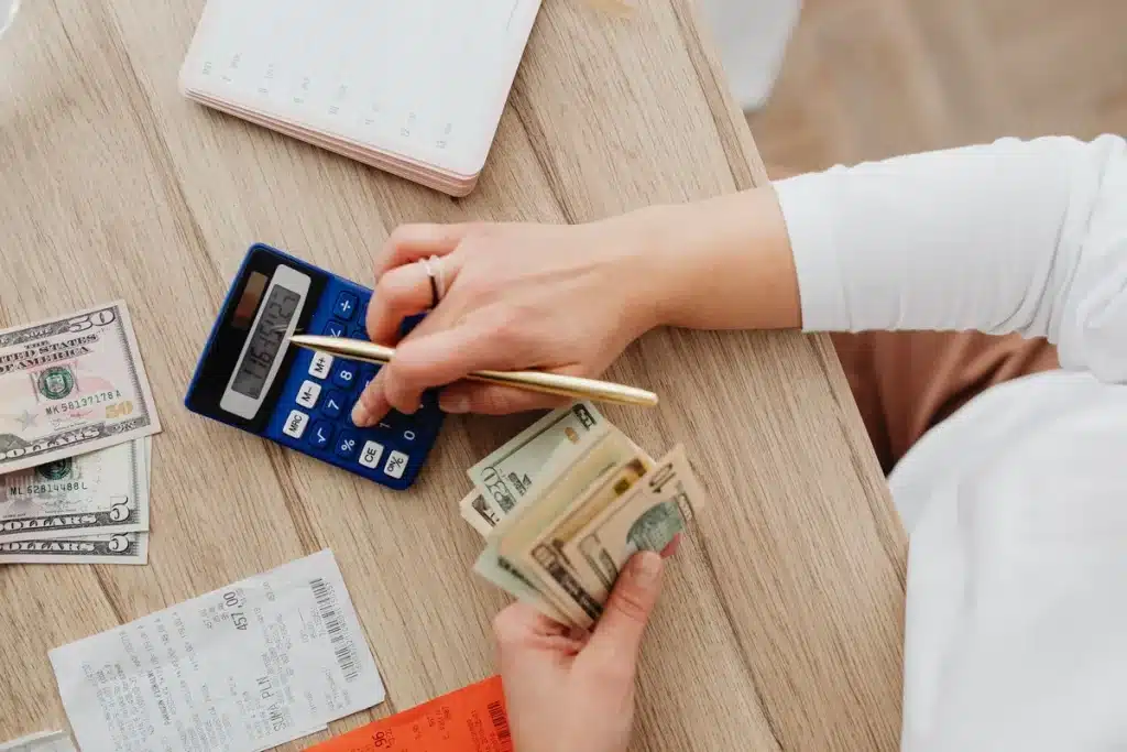 Personne calculant son budget mensuel face à des factures et relevés bancaires