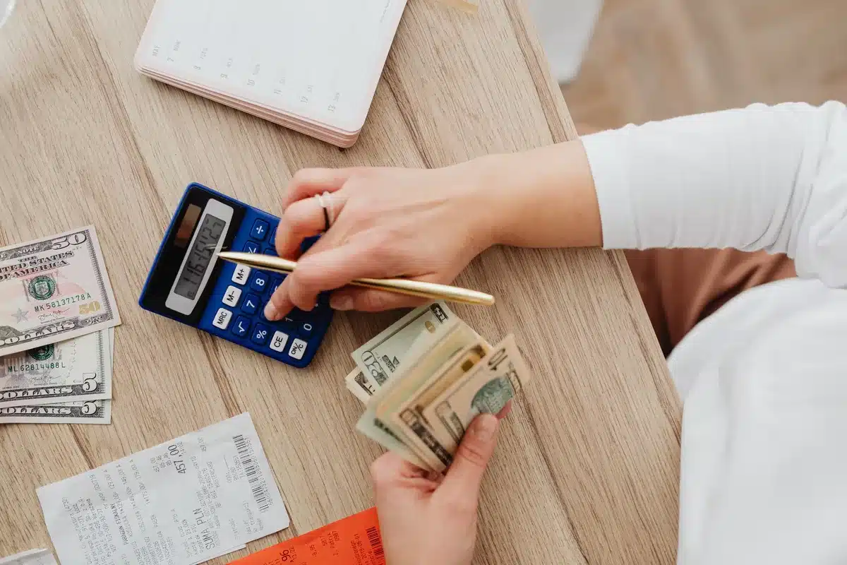 Personne calculant son budget mensuel face à des factures et relevés bancaires