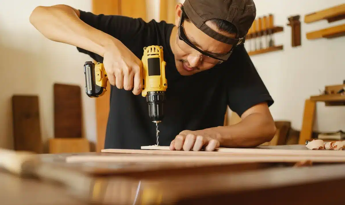 Mains tenant une perceuse au-dessus d'une surface en bois dans un intérieur résidentiel