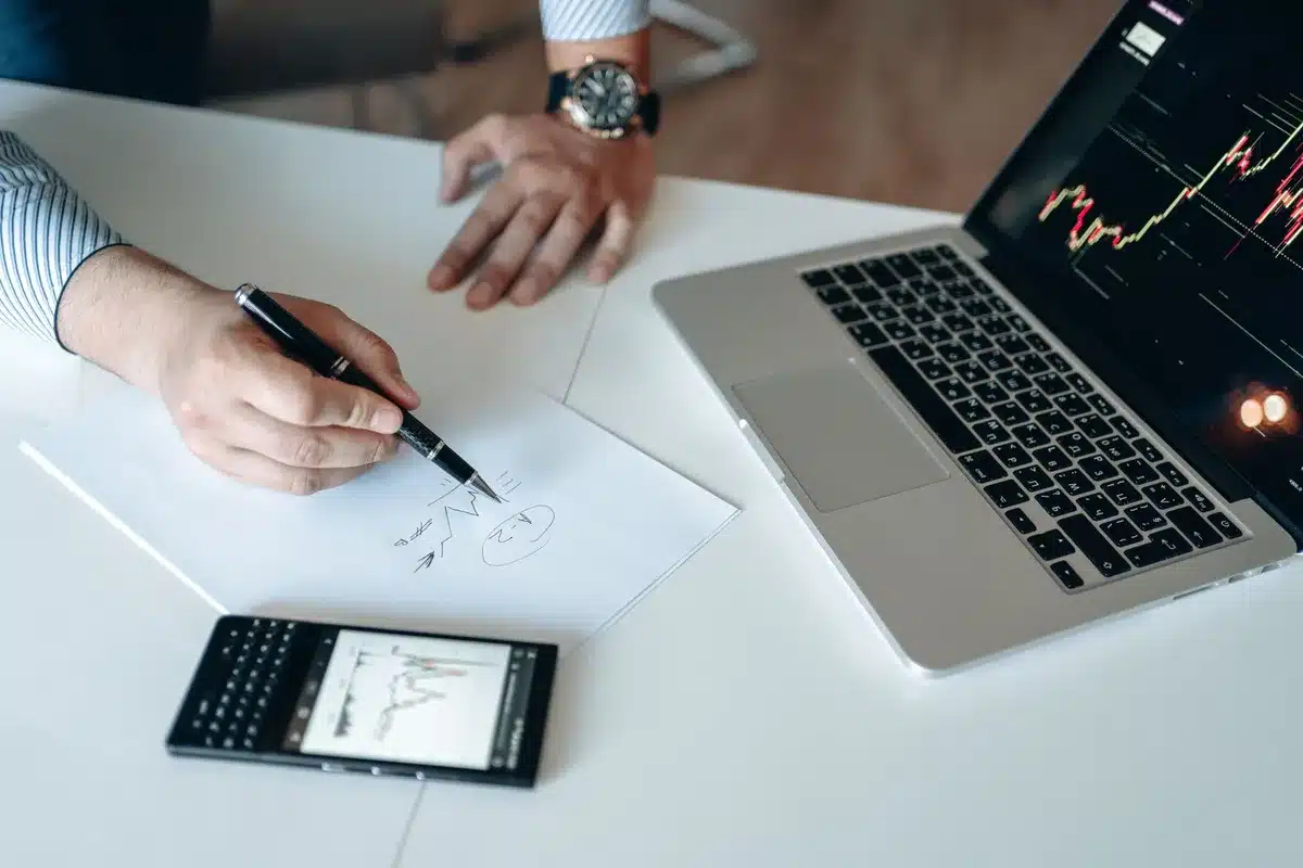Mains d'une personne devant un écran d'ordinateur affichant des graphiques de trading et des symboles crypto