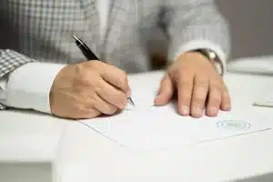Mains signant des documents de transfert de retraite avec calculatrice et relevés financiers sur un bureau