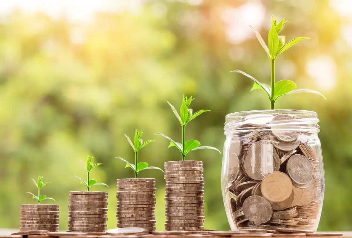 Mains versant des pièces dans une tirelire transparente, symbolisant l'investissement solidaire.