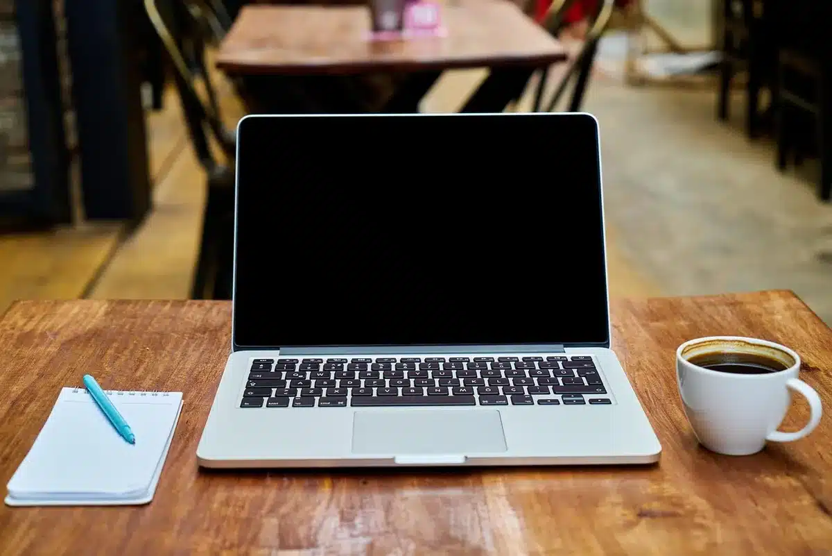 Bureau lumineux avec ordinateur affichant du code et carnet, mains au clavier