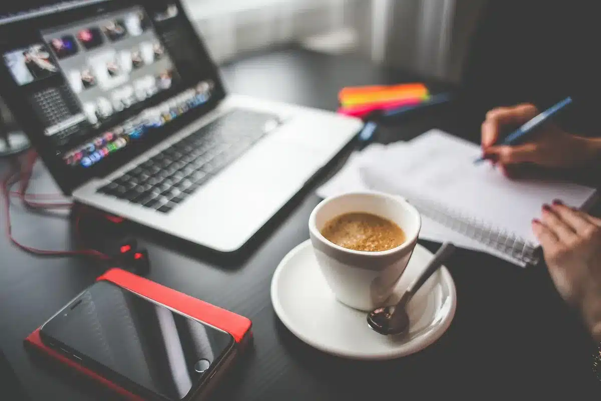 Carnet ouvert, smartphone et tasse de café sur une table de terrasse, prise de notes anonymes