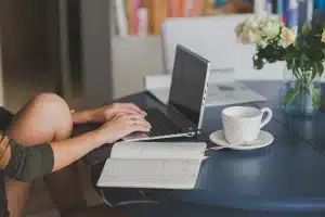 Bureau lumineux avec ordinateur affichant un fil social, bloc‑notes et tasse de café