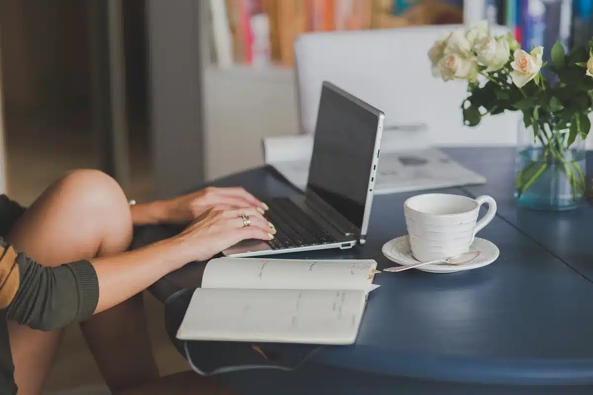 Bureau lumineux avec ordinateur affichant un fil social, bloc‑notes et tasse de café