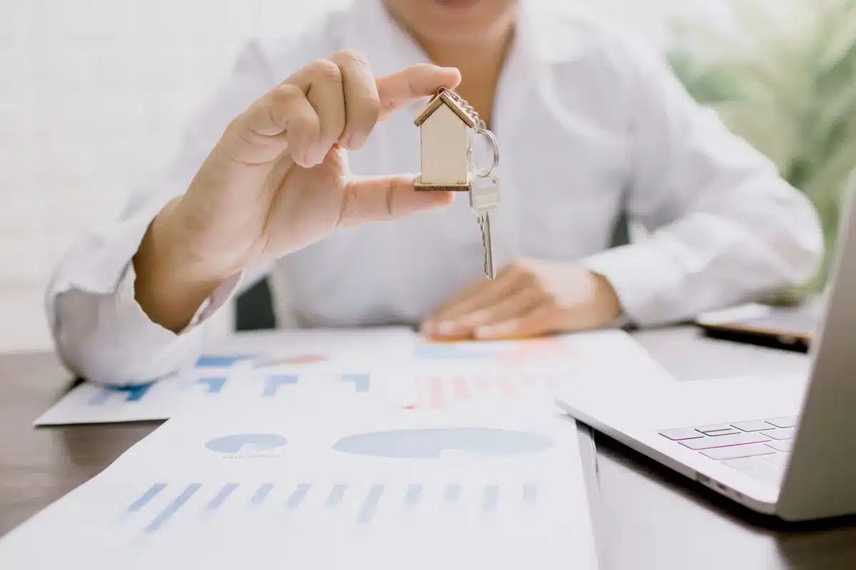 Hands filling mortgage application next to keys and a calculator on a tidy desk, documents visible but unreadable