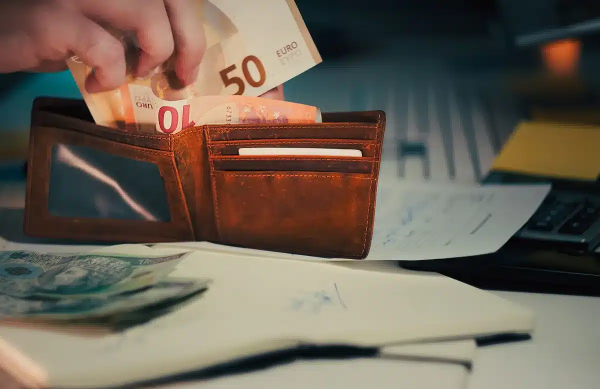 A neat pile of loan documents, a pair of anonymous hands signing a form with a pen, and a small blurred stack of coins in the background