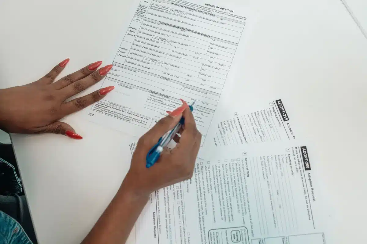 Close-up of hands filling a housing allowance form with a pen, a neutral desk surface with no logos