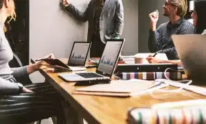 Équipe anonyme en réunion dans un bureau baigné de lumière, laptop et schémas sur la table