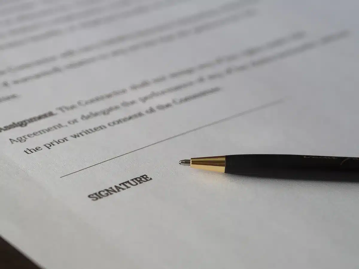 Personne signant un acte de donation sur une table, documents et stylo visibles