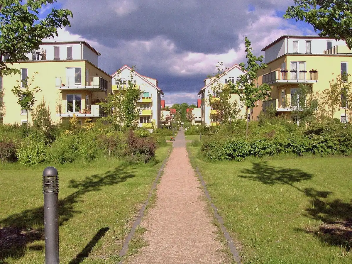 Sunlit street view of a generic new residential building with balconies and small green spaces