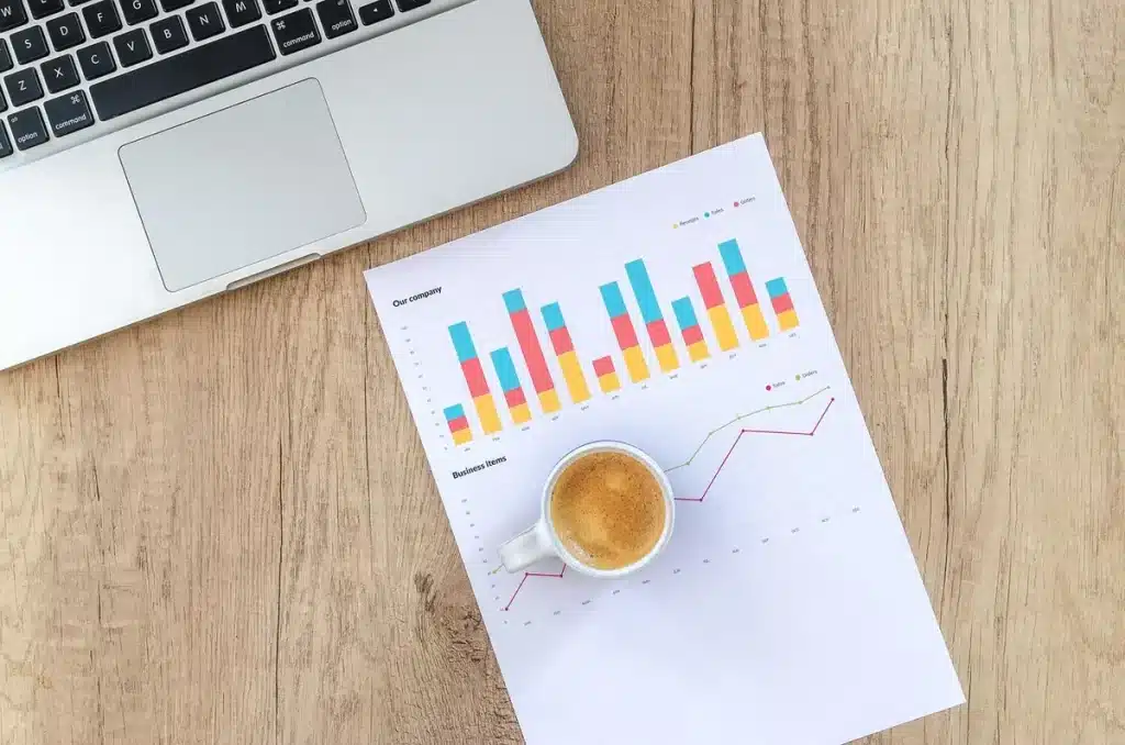 Table de réunion en journée avec documents, ordinateur et mains anonymes pointant un graphique