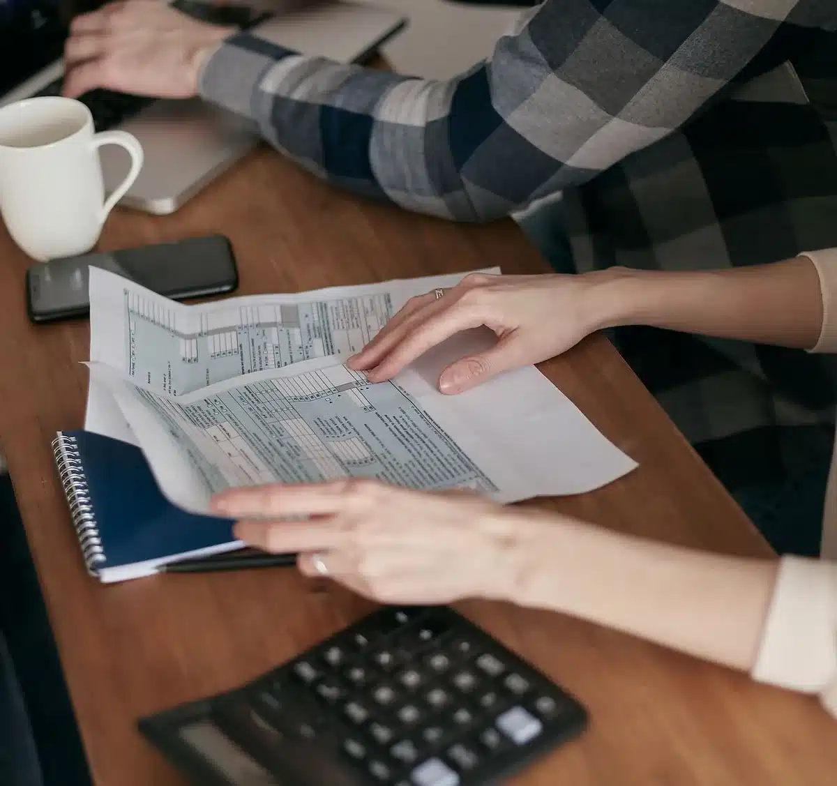 Hands filling a tax form at a tidy desk with a calculator and blurred documents in the background